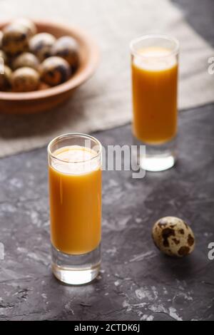 Süßer Eierlikör im Glas mit Wachteleiern auf schwarzem Betongrund. Seitenansicht, Low-Key, Nahaufnahme. Stockfoto