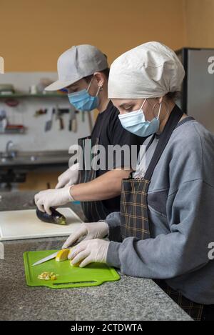 Vertikale Aufnahme von zwei jungen Köchen schneiden Gemüse tragen medizinische Masken Stockfoto