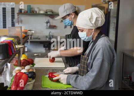 Zwei junge Köche schneiden Gemüse in medizinischen Masken Stockfoto