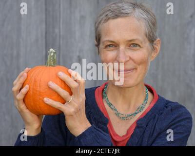 Die kaukasische kanadische Landsfrau mittleren Alters mit kurzen Haaren hält einen Kürbis in den Händen und schaut auf die Kamera. Stockfoto
