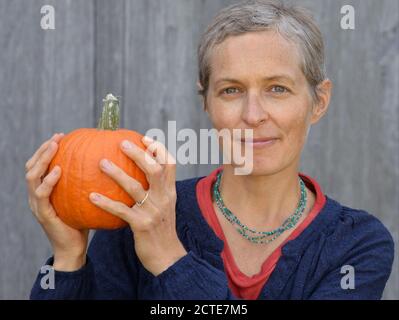 Die kaukasische kanadische Landsfrau mittleren Alters mit kurzen Haaren hält einen Kürbis in den Händen und schaut auf die Kamera. Stockfoto