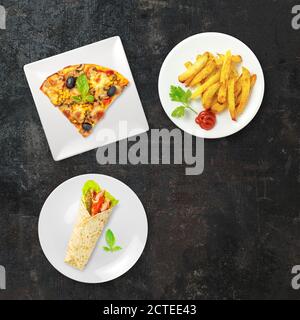 Draufsicht auf Fast-Food-Gerichte auf dunkler Oberfläche. Pizza, Tortilla und Pommes auf schwarzem Hintergrund mit Kopierfläche isoliert. Ungesunde Lebensmittel. Zusammensetzung Stockfoto