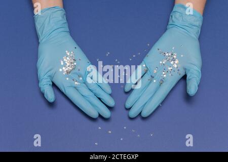 Hände in medizinischen Handschuhen auf blauem Hintergrund. Glitter kleine Sterne in den Händen. Weihnachts- und Neujahrskarte Konzept. Foto von oben, Kopierbereich. Stockfoto