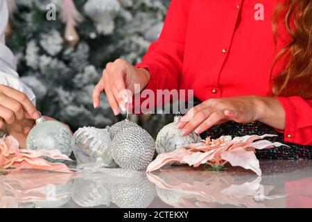 Nahaufnahme einer Anordnung von Weihnachtskugeln und anderen Ornamenten auf einem Tisch mit weiblichen Händen. Weihnachtsfeiertage und Dekorationskonzept. Stockfoto