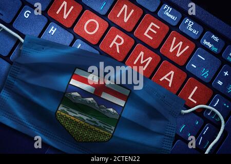 COVID-19 Coronavirus neues normales Konzept in der kanadischen Provinz Alberta wie gezeigt von Alberta Flagge auf Gesichtsmaske mit Neue normale auf Laptop rote Warnung Stockfoto