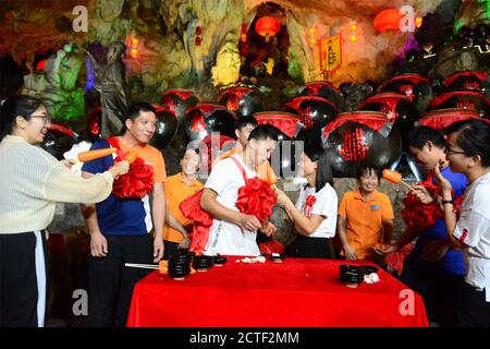 Indem sie Spiele spielen und sich mit roten Blumen kleiden, versuchen über 1500 Paare, die von der Aktivität angezogen wurden, traditionelle chinesische Hochzeitszeremonie in einem Ka Stockfoto
