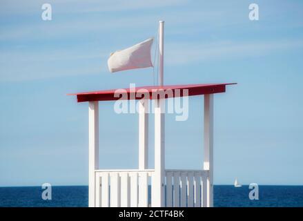 Leerer Holzturm für Rettungsschwimmer mit einem flatternden Beutel mit weißer Flagge. Ein Segelboot und Adria im Hintergrund Stockfoto