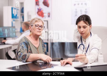 Arzt spricht über Knieschmerzen mit älteren Patienten hält Radiographie im Krankenhaus Büro . Medic trägt weißen Mantel arbeiten am Computer. Stockfoto