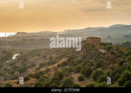 Tal der Tempel: Tempel der Concord vor der industriellen Landschaft im Hintergrund bei Sonnenuntergang. Agrigento, Sizilien, Italien. Stockfoto