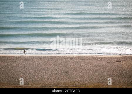 Mann, der während eines angenehmen spätsommerlichen Sonnenaufgangs an einem Schwarzmeerstrand spazierengeht. Stockfoto