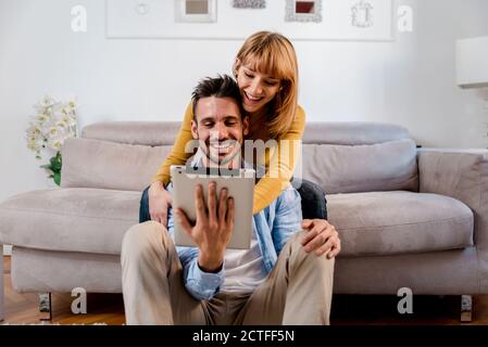Glückliche paar Millennials mit digitalen Tablet zu Hause. Freund und Freundin sitzen auf dem Sofa im Wohnzimmer auf der Suche nach etwas auf Inter Stockfoto