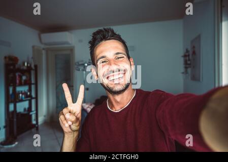 Glücklich gut aussehende junge Mann nimmt ein Selfie zu Hause - Positiver Typ lächelt bei der Kamera drinnen Stockfoto