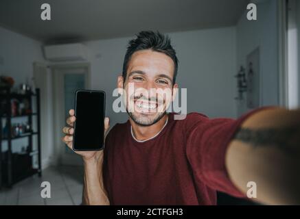 Glücklich gut aussehende junge Mann nimmt ein Selfie zu Hause - Positiver Typ lächelt bei der Kamera drinnen Stockfoto