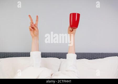 Hände halten rote Tasse und V-Zeichen stehen unter Die Decke Stockfoto