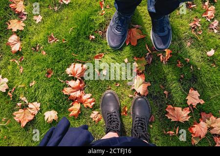 Männliche und weibliche Beine in Sneakers und Stiefeln stehen auf Boden mit gelben Herbstblättern Stockfoto