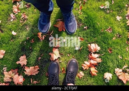 Männliche und weibliche Beine in Sneakers und Stiefeln stehen auf Boden mit gelben Herbstblättern Stockfoto