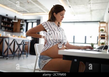 Müde schwangere Frau von zu Hause aus arbeiten am Computer Stockfoto