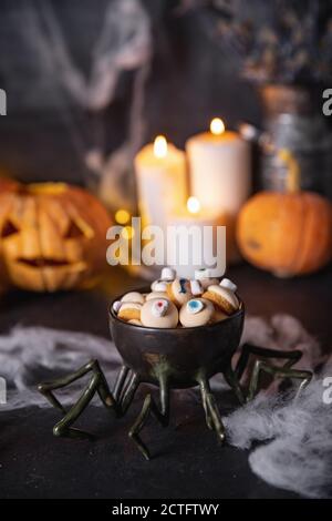 Süßigkeiten und Kekse in Form eines Auges für den Urlaub an halloween, dunkler Hintergrund mit Spinnweben, Kürbisse und Kerzen Stockfoto
