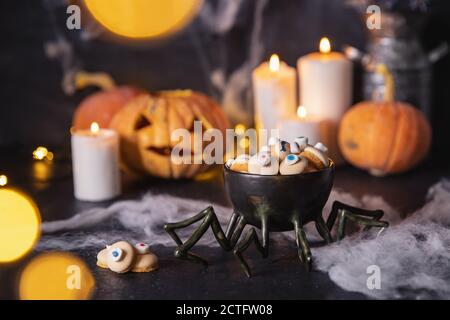 Süßigkeiten und Kekse in Form eines Auges für den Urlaub an halloween, dunkler Hintergrund mit Spinnweben, Kürbisse und Kerzen Stockfoto