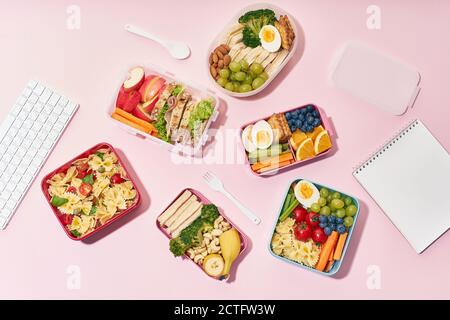 Draufsicht auf Schullunchboxen mit verschiedenen gesunden und nahrhaften Mahlzeiten Auf rosa Hintergrund Stockfoto