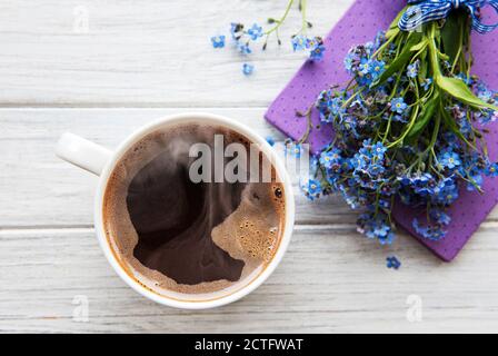 Blaue Vergissmeinnicht-Blumen, Notizbuch und eine Tasse heißen Kaffee. Das Konzept der Feiertage und Guten Morgen Wünsche. Stockfoto