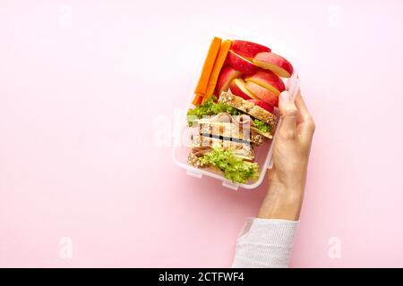 Frau hält ein Schulessen Draufsicht. Gesunde nahrhafte Mahlzeit in Behälter von oben mit Kopieplatz auf rosa Hintergrund Stockfoto