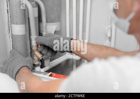 Männliche Klempner in medizinische Maske prüft Rohre für zentrale heiß Und Kaltwasserversorgung der Wohnung Stockfoto