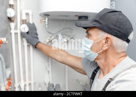 Männliche Klempner in medizinische Maske prüft Rohre für zentrale heiß Und Kaltwasserversorgung der Wohnung Stockfoto