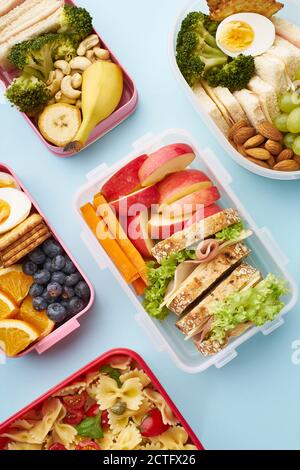 Draufsicht auf Schullunchboxen mit verschiedenen gesunden und nahrhaften Mahlzeiten Auf blauem Hintergrund Stockfoto
