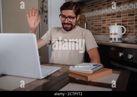 Junger Mann mit Videoanruf über Computer im Heimbüro. Virtuelle Hausfeier. Online-Teambesprechung Videokonferenzanrufe von zu Hause aus, Kommunikation Stockfoto