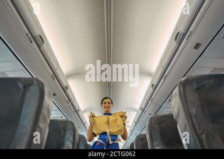 Positive Stewardess demonstriert Lebensweste in Flugzeugkabine Stockfoto