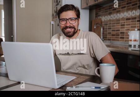 Zufrieden mit der geleisteten Arbeit. Glücklicher junger Mann, der am Laptop arbeitet, während er an seinem Arbeitsplatz im Heimbüro sitzt. Glücklicher Mitarbeiter, kein Stress, entspannen Stockfoto