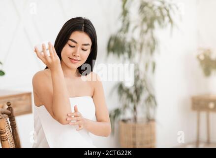 Hübsche asiatische Dame in Handtuch feuchtigkeitsspendend ihren Ellbogen gewickelt Stockfoto