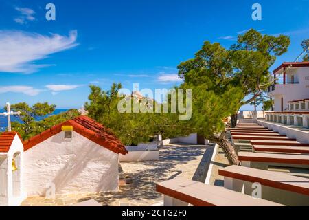 Kleine Rote Kirche von Panagia Lamiotissa mit großer Sitzecke für Feiern mit Blick auf große Kreuz auf einem Hügel auf der Insel Karpathos, Griechenland Stockfoto