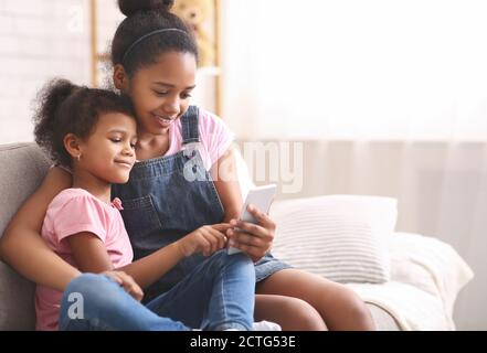 Kleines afroamerikanisches Mädchen, das auf dem Handy ihrer Schwester spielt Stockfoto