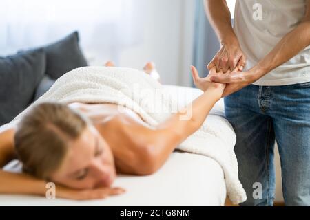 Professionelle Masseur tun therapeutische Massage. Frau genießt Massage in ihrem Haus. Junge Frau bekommen entspannende Körpermassage. Stockfoto