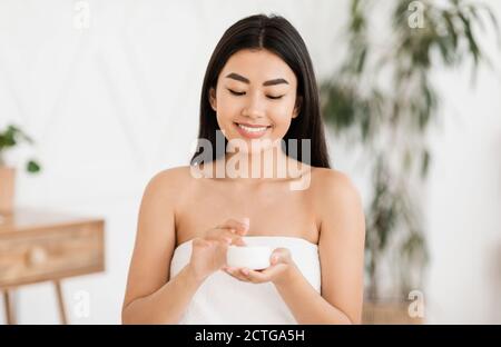 Glückliche asiatische Dame in Handtuch mit Sahne eingewickelt Stockfoto