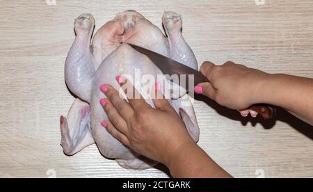 Eine Top-Nahaufnahme einer Frau, die auf einem Holzbrett das ganze Huhn schneidet. Pinke Fingernägel. Stockfoto