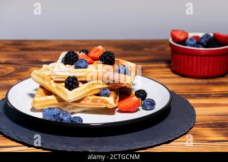 Belgische Waffeln gekrönt mit verschiedenen Beeren bereit zum Essen auf Holzhintergrund Stockfoto