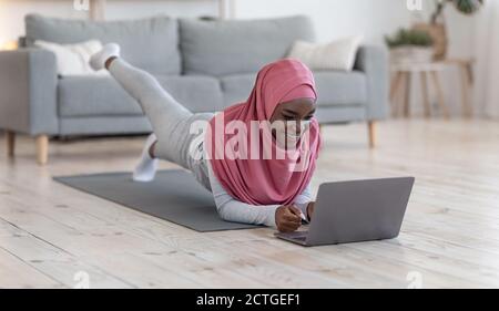 Sportliche schwarze muslimische Frau tut Planke vor dem Laptop Zu Hause Stockfoto