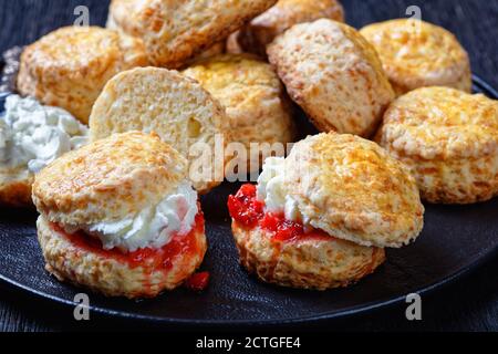 Nahaufnahme von Scones im englischen Stil mit gerinnter Sahne und Erdbeermarmelade auf einem schwarzen Teller, Landschaftsansicht von oben Stockfoto