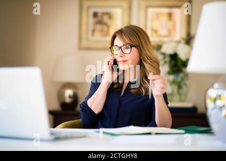 Selbstbewusste Geschäftsfrau, die von zu Hause aus geschäftlich telefonieren kann. Heimbüro. Stockfoto