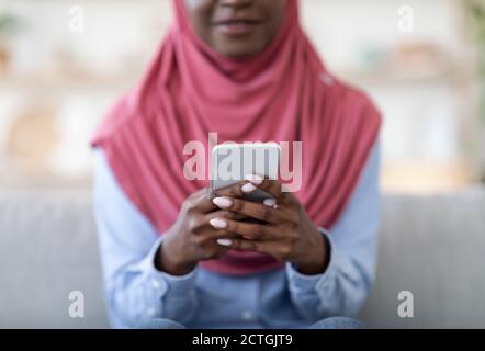 Nützliche App Unkenntlich schwarze muslimische Dame mit modernen Smartphone zu Hause, Nahaufnahme