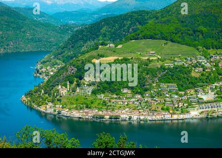 Luftaufnahme über Morcote mit Alpensee Lugano und Berg an einem sonnigen Tag im Tessin, Schweiz. Stockfoto