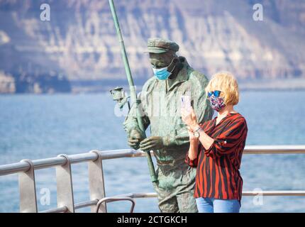 Las Palmas, Gran Canaria, Kanarische Inseln, Spanien. September 2020. Ein Tourist mit Gesichtsbedeckung (die in Spanien obligatorisch sind) macht ein Selfie neben einer Statue eines lokalen Fischers, ebenfalls mit Gesichtsmaske, in Las Palmas auf Gran Canaria. Aufgrund der derzeitigen Spitzengruppe neuer Coronavirus-Fälle in Spanien und den kanarischen Inseln haben Großbritannien und Deutschland Spanien und die Kanarischen Inseln auf ihre Quarantäneliste gesetzt. Kredit: Alan Dawson/Alamy Live Nachrichten Stockfoto