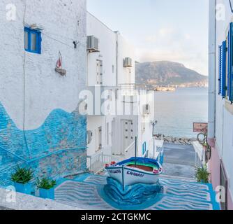 Pigadia, Karpathos, Griechenland - 4. Oktober 2019: Beliebter touristischer Fotoplatz in Pigadia Stadt mit farbiger Treppengasse und Boot in der Mitte, Morgen Stockfoto