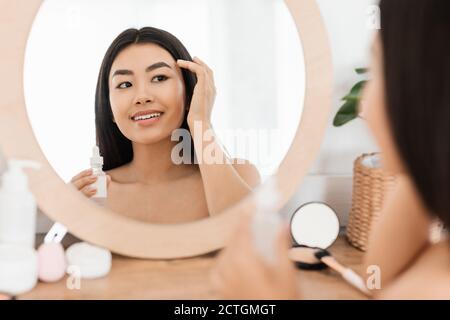 Lächelnde asiatische junge Frau Anwendung Gesichts-Serum Stockfoto