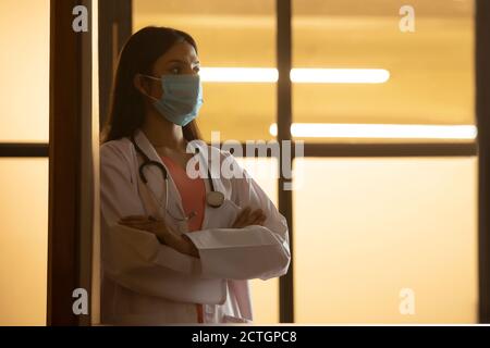 Arzt im Mantel, der mit einer Gesichtsmaske aufsteht Stockfoto