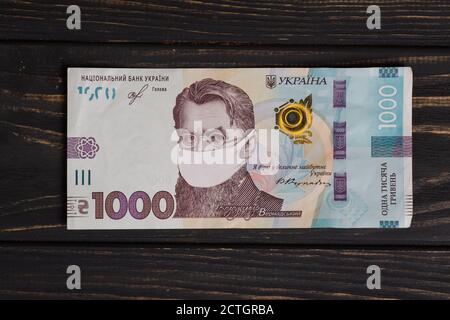 Coronovirus Krise Konzept - Geld der Ukraine mit Schutzmaske. ukrainische Griwna Banknoten auf Holztisch. Griwna 1000 uah Stockfoto