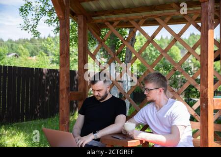 Ein paar Freunde, die auf Laptop auf dem Hintergrund aus Holz Pergola-Gitter Stockfoto